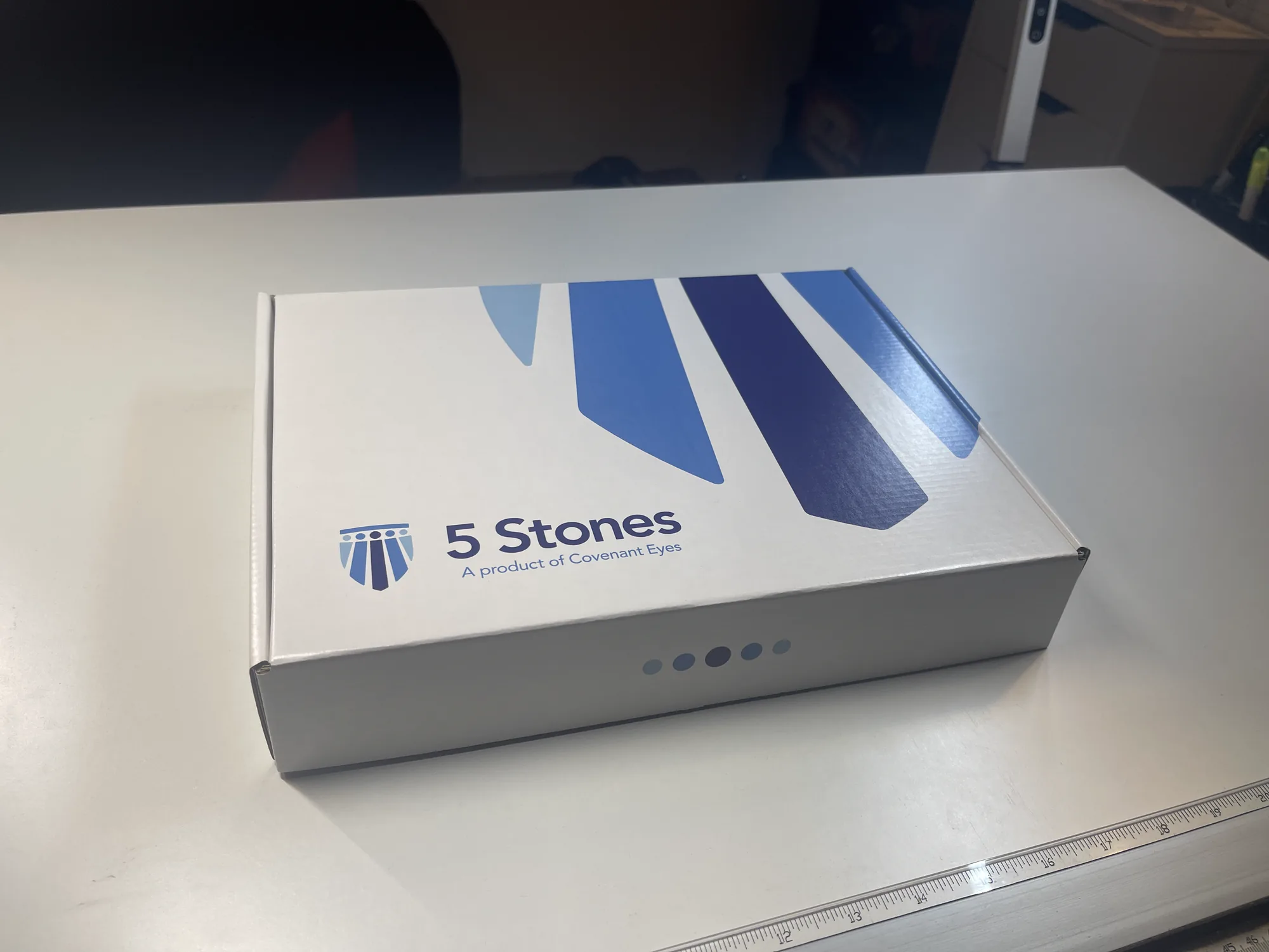 The shipped kit closed on a desk, seen at a three-quarter angle, five dots along the front edge.