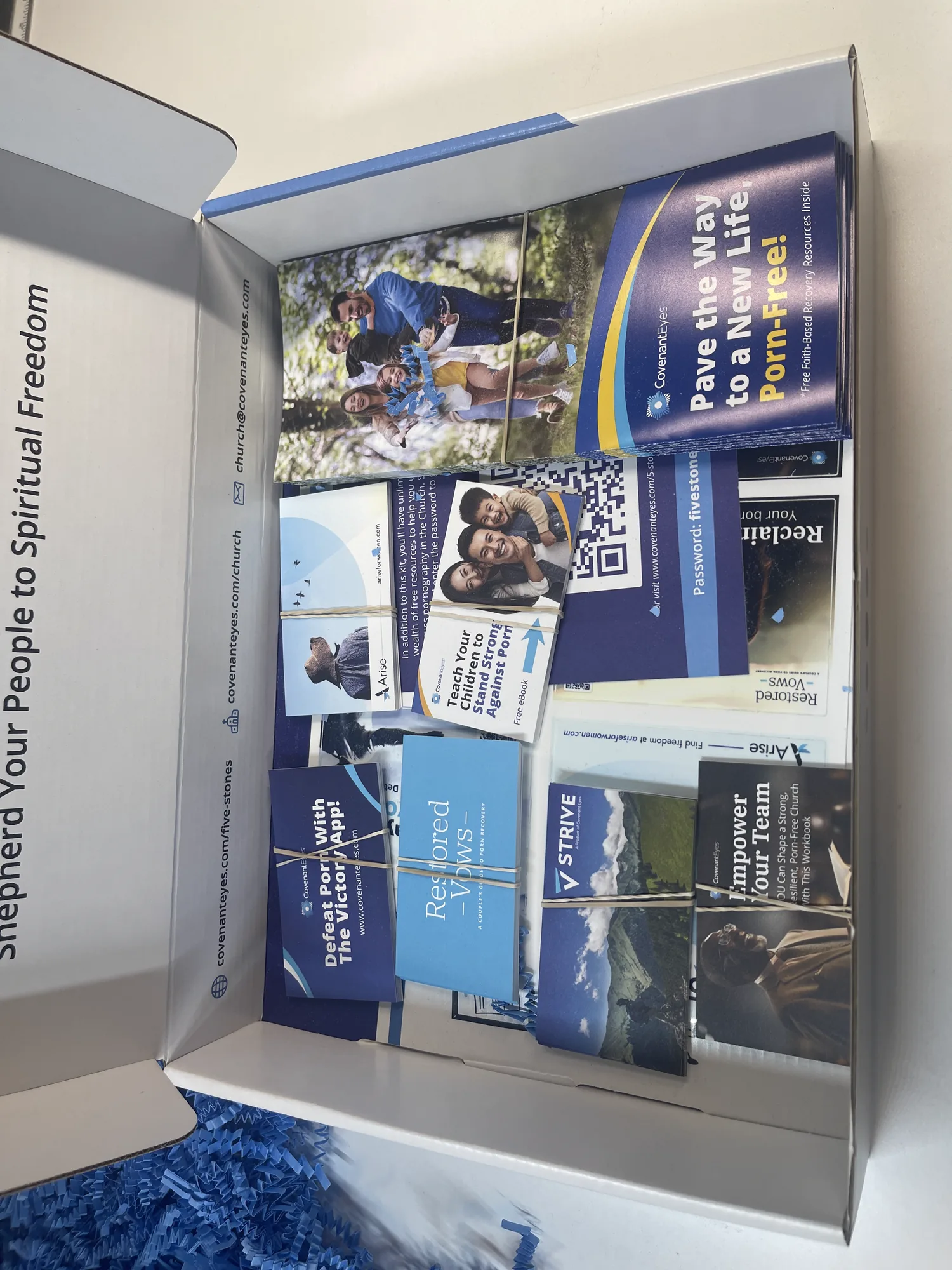 The shipped 5 Stones kit open on a studio desk, the tray packed with the gatefold brochure and the resource cards, the interior lid printed &ldquo;Shepherd Your People to Spiritual Freedom&rdquo;.